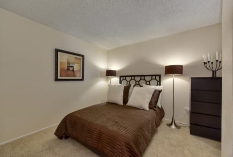 Furnished Bedroom with queen size bed, tall dresser and two floor lamps.  Room is carpeted and with beige paint.